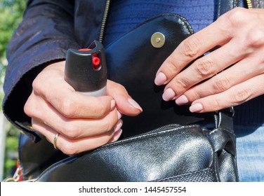 A young woman pulls a can of tear gas or bottle of pepper spray out of her purse. Means of self-defense. Selective focus, close-up. 