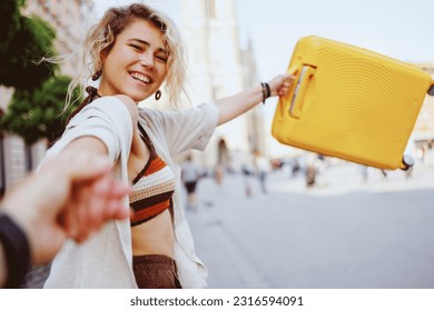 Young woman pulls her boyfriend's hand and holds a traveling bag while exploring the city - Shutterstock ID 2316594091