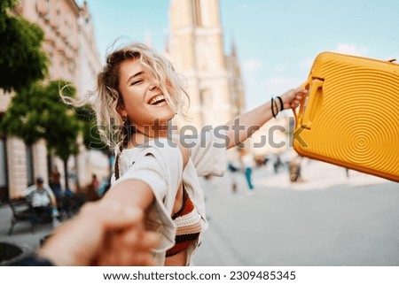 Young woman pulls her boyfriend's hand and holds a traveling bag while exploring the city