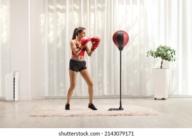 Young Woman Punching A Free Standing Boxing Bag At Home