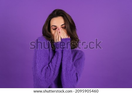 Young woman in a purple soft cozy sweater on the background is cute, in high spirits, laughs shyly, covering her mouth with her hands