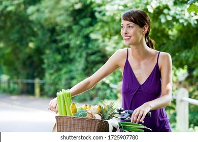 A Young Woman Pushing A Bicycle With A Basket Full Of Shopping