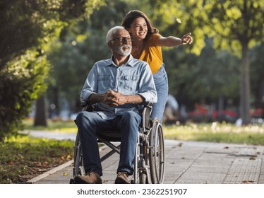 Young woman pushing smiling senior man in wheelchair in park - Powered by Shutterstock