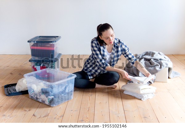 A young woman puts away seasonal\
clothes and items for storage in boxes. Spring\
cleaning.