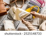 A young woman puts fashionable, beautiful bags into fabric bags for neat seasonal storage. Home wardrobe. Putting things in order. Lots of trendy, stylish bags and accessories.