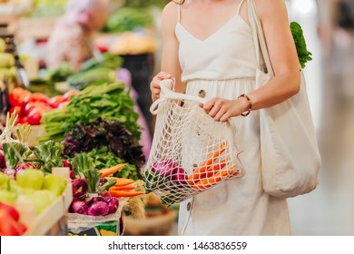 Young Woman Puts Fruits And Vegetables In Cotton Produce Bag At Food Market. Reusable Eco Bag For Shopping. Zero Waste Concept.