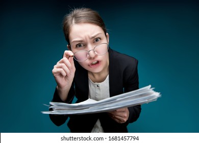 A young woman puts glasses on her nose and looks in camera with angry surprise. Director dissatisfied with paperwork or errors in them. Teacher screams at pupil