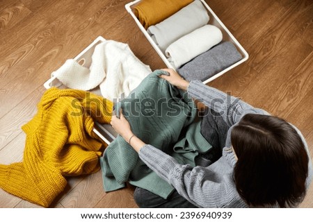 A young woman puts knitted clothes into a metal laundry basket. The concept of restoring order, cleaning, cluttering, organizing space.