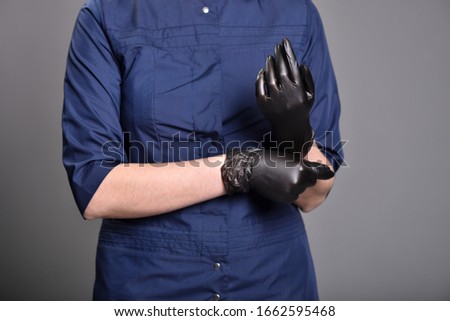Young woman puts on black latex gloves before procedures. Close-up