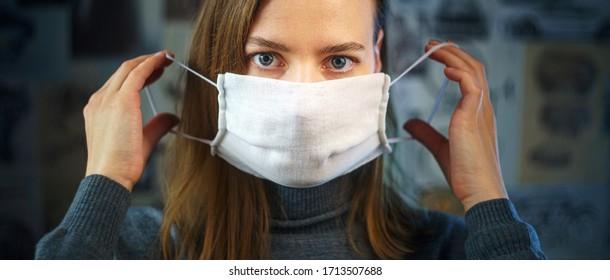 A young woman puts on a gauze mask before leaving home and looking at the camera. Preventive fight against viral infection- coronavirus COVID-19. Health protection concept.