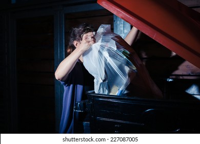 A Young Woman Is Putting A Bag Of Rubbish In A Large Bin At Night