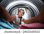 Young woman putting clothes into washing machine in bathroom, view from inside