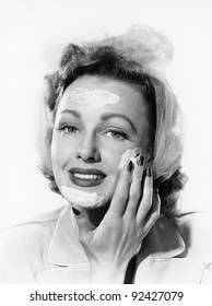 Young woman putting cream onto her face