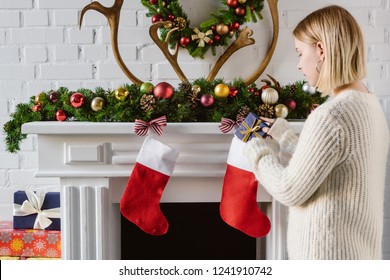 Young Woman Putting Gift In Christmas Stocking At Fireplace