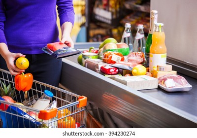Young woman putting goods on counter in supermarket