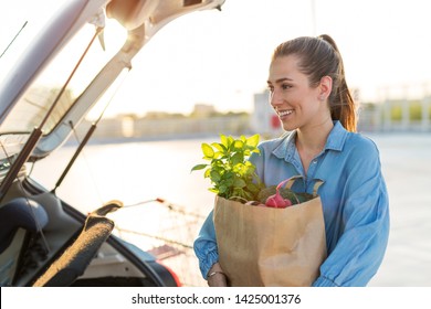 Young Woman Putting Groceries At The Car Trunk