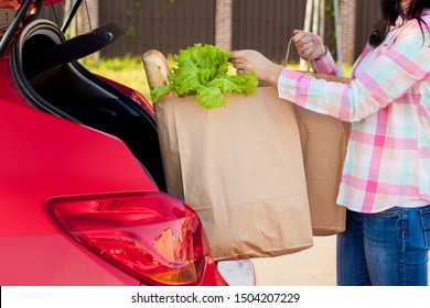 Young woman putting groceries from a supermarket in paper bags into the trunk of a car. Shopping mall collection, holiday shopping, shopping, small businesses, retail shopping concept