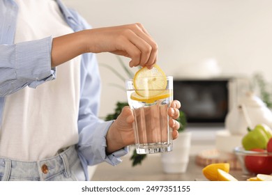 Young woman putting lemon slice into glass of water in kitchen, closeup - Powered by Shutterstock