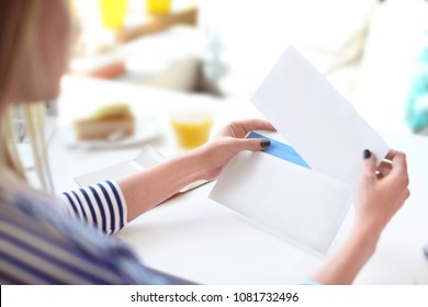 Young woman putting letter into envelope at table in cafe. Mail delivery