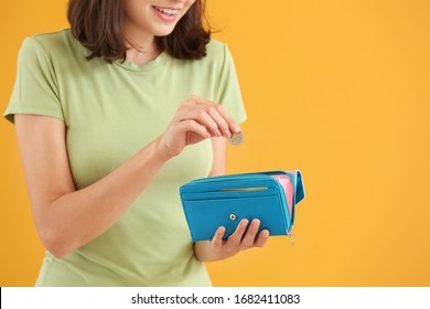 Young Woman Putting Money In Wallet On Color Background