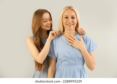 Young woman putting necklace around her mother's neck on grey background