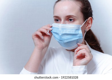 Young woman putting on face mask on a gray background. Caucasian female adjusts the protective mask with her hands. - Powered by Shutterstock