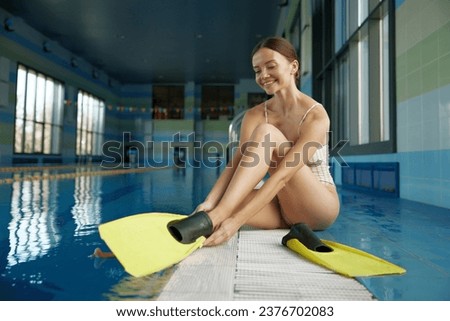 Young woman putting on flippers preparing for training class at pool