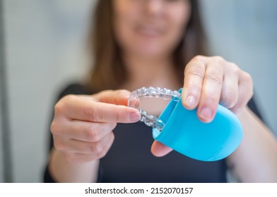 Young woman putting with two fingers an invisible dental aligner inside a case while smiling - Shutterstock ID 2152070157