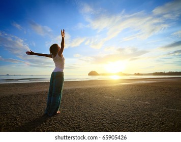 Junge Frau mit hohen Händen, die auf Sand stehen und einen Himmel sehen