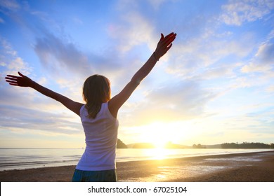 Young woman with raised hands standing on wet sand and looking to a horizon