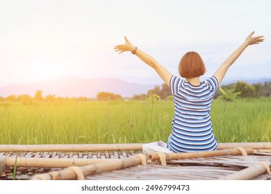 A young woman raises both her hands above her head to invoke God's blessing with the faith and power she has for God on the blurry background of a green rice field in the morning. - Powered by Shutterstock