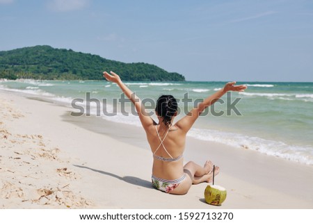 Young woman raising arms and celebrating her great vacation on the beach with white sand and clean sea