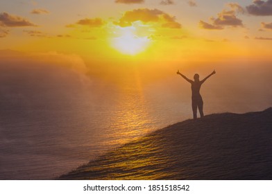 Young woman raising her arms up to the sunset sky feeling happy, and full of joy. 