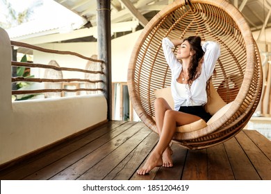 Young woman in the rattan lounge hanging chair at the balcony with green nature tropical background.