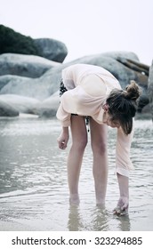 Young Woman Reaching Down To Touch The Sand At A Quiet Beach 