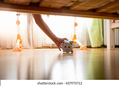 Young Woman Reaching Under The Bed For Alarm Clock