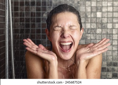 Young Woman Reacting In Shock To Hot Or Cold Shower Water As She Stands Under The Shower Head Washing Her Hair Eyes Closed With Her Hands Raised And Mouth Open