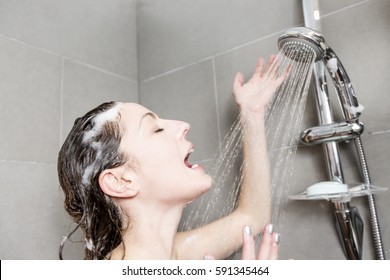 Young Woman Reacting In Shock To Hot Or Cold Shower Water As She Stands Under The Shower Head Washing Her Hair Looking At The Camera With Her Hands Raised And Mouth Open