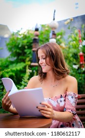 Young Woman Reading In A Blank Magazine While Sitting In The Garden.