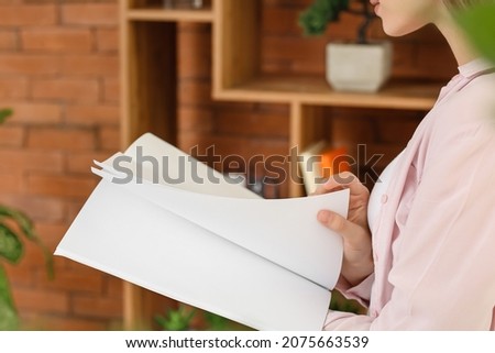 Young woman reading blank magazine in room