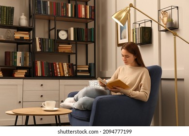 Young Woman Reading Book In Armchair Indoors. Home Library