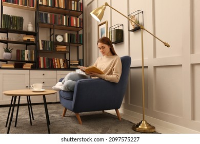 Young Woman Reading Book In Armchair Indoors. Home Library