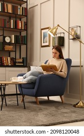 Young Woman Reading Book In Armchair Indoors. Home Library