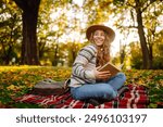 Young woman reading book at autumn park. Concept of autumn walks, relax, nature, picnic.