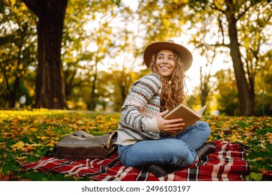 Young woman reading book at autumn park. Concept of autumn walks, relax, nature, picnic. - Powered by Shutterstock