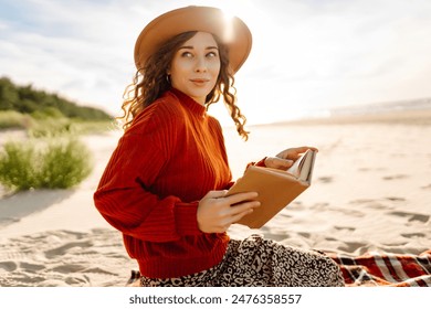 Young woman reading a book by the sea at sunset. Woman relaxing on beach. The concept of relaxation, enjoyment, solitude with nature - Powered by Shutterstock