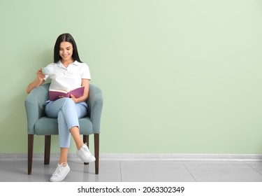 Young woman reading book and drinking coffee while relaxing in armchair at home