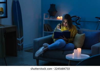 Young woman reading book with flashlight at home during blackout - Powered by Shutterstock