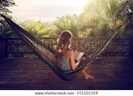 Young woman reading a book in a hammock on the terrace in the jungle at sunset