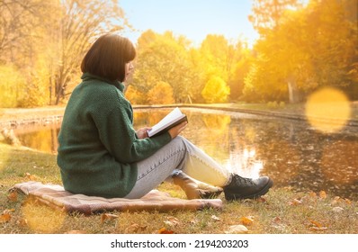 Young Woman Reading Book Near Pond In Autumn Park